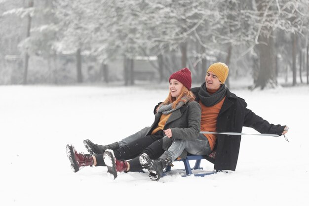 Colpo lungo delle coppie che si siedono sulla slitta in inverno