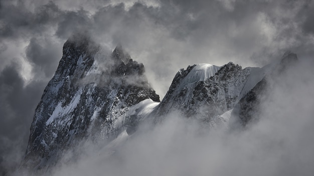 Colpo magico di un bellissimo picco di montagna innevata coperto di nuvole.