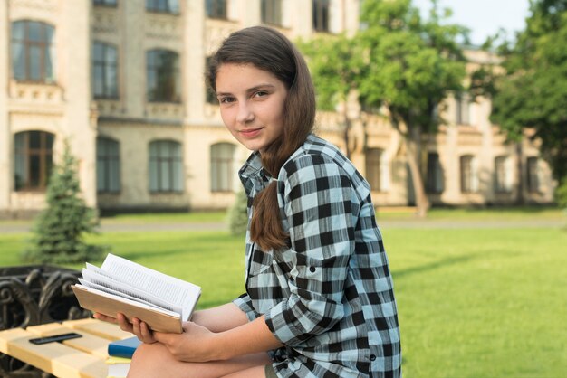 Colpo medio di vista laterale dell&#39;adolescente che tiene libro aperto