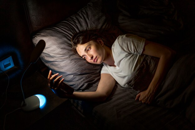 Colpo medio donna a letto con lo smartphone