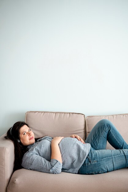 Colpo medio donna incinta posa sul divano