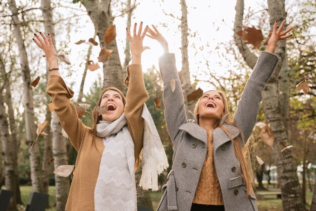 Colpo medio due donne che giocano con le foglie nel parco