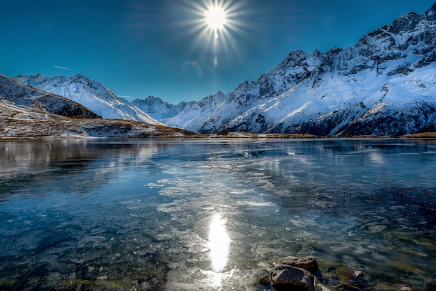 Colpo mozzafiato di un bellissimo lago ghiacciato circondato da montagne innevate durante una giornata di sole