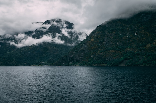 Colpo mozzafiato di un lago circondato dalle montagne innevate sotto il cielo nebbioso in Norvegia