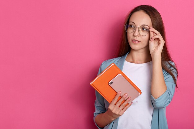 Colpo orizzontale della femmina pensierosa con l'organizzatore e il telefono arancio in mani