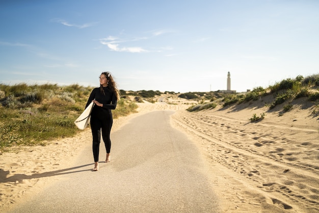 Colpo poco profondo del fuoco di una femmina attraente che trasporta una tavola da surf