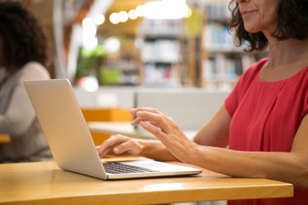 Colpo potato della donna caucasica che lavora con il computer portatile alla biblioteca