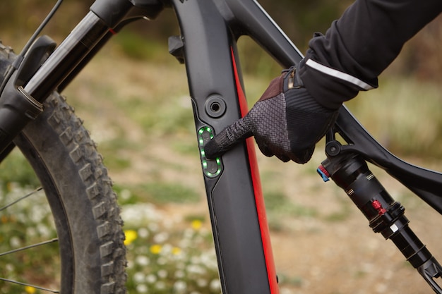 Colpo potato della mano maschio in guanto nero premendo il pulsante con il dito indice sul pannello di controllo sulla bici electirc. Motociclista che cambia modalità di velocità prima di guidare la sua bicicletta del ripetitore motorizzata in salita