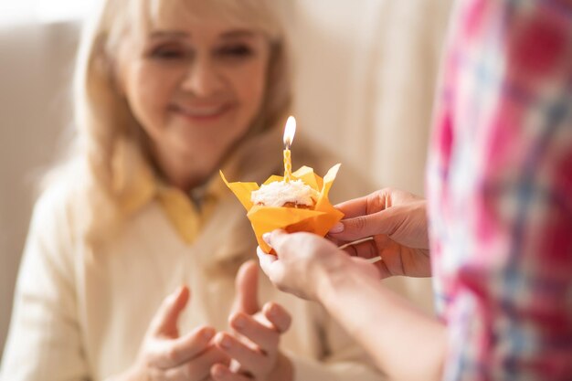 Colpo ravvicinato di una gustosa cupcake in un involucro arancione che viene dato alla madre anziana mentre la candela di compleanno sta bruciando