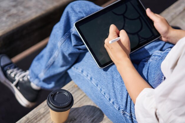 Colpo ritagliato di mani femminili che disegnano su tavoletta grafica digitale con penna seduta con una tazza di caffè o