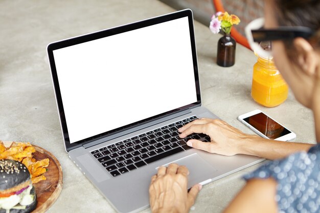Colpo ritagliato di successo imprenditrice femminile in vacanza utilizzando il computer portatile, controllo e-mail, amici di messaggistica online, seduto al caffè con il taccuino aperto