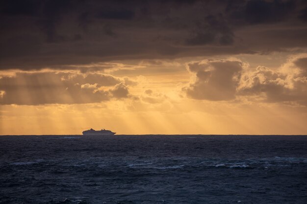 Colpo sbalorditivo dell'oceano blu calmo e della sagoma di una nave sotto un cielo nuvoloso durante il tramonto