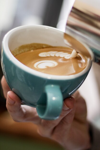 Colpo selettivo verticale del primo piano di caffè con arte del latte in una tazza ceramica blu su una superficie di legno