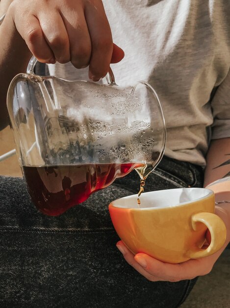 Colpo selettivo verticale del primo piano di un tè di versamento della persona in una tazza ceramica gialla