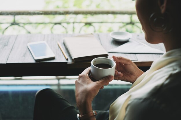 Colpo superiore della donna irriconoscibile che si siede sul balcone e che tiene tazza di caffè