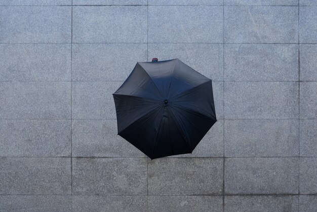 Colpo superiore della persona irriconoscibile che sta sotto l'ombrello su pavimentazione