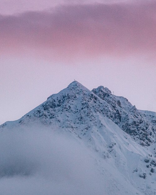 Colpo verticale del picco di montagna innevato sotto il cielo nuvoloso variopinto