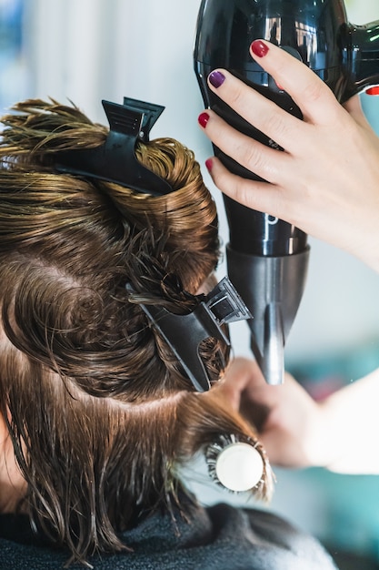 Colpo verticale del primo piano di un parrucchiere che asciuga i capelli corti di una donna in un salone di bellezza