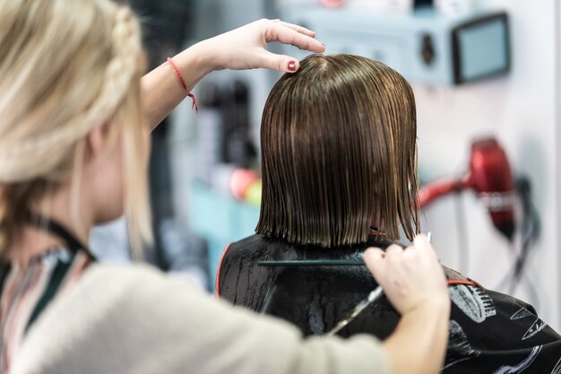 Colpo verticale del primo piano di un parrucchiere che taglia i capelli corti di una donna in un salone di bellezza