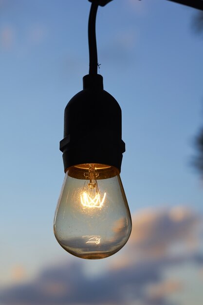 Colpo verticale del primo piano di una lampadina accesa contro il cielo nuvoloso