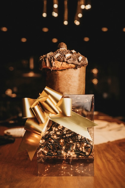 Colpo verticale del primo piano di una scatola romantica con luci, un nastro dorato e un muffin