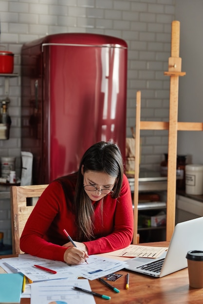 Colpo verticale dell'interno della femmina fa la relazione finanziaria, pone alla cucina accogliente con il frigorifero in background.