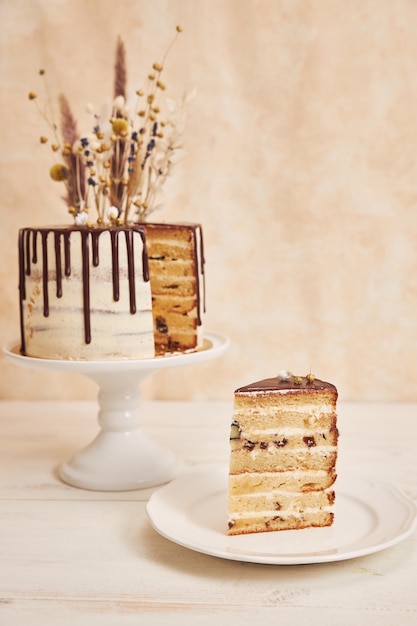 Colpo verticale della deliziosa torta Boho con gocce di cioccolato e fiori in cima con decorazioni dorate