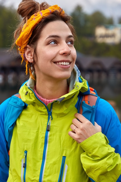 Colpo verticale della donna caucasica positiva distoglie lo sguardo, passeggia e respira aria fresca