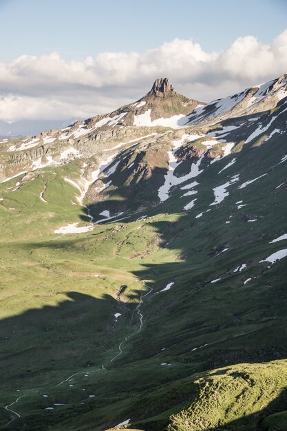 Colpo verticale delle colline erbose vicino ad una montagna nevosa con un cielo nuvoloso