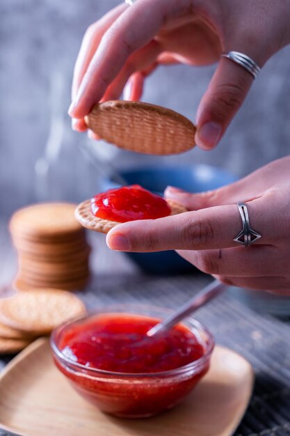 Colpo verticale delle mani che fanno il biscotto Maria fresco (galletas Maria) con marmellata di fragole