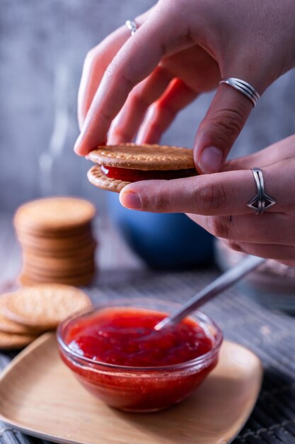 Colpo verticale delle mani che tengono il biscotto Maria fresco (galletas Maria) con marmellata di fragole