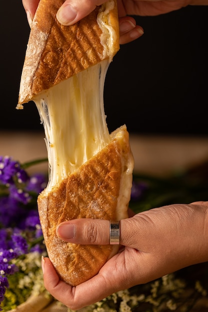 Colpo verticale delle mani di una persona che tengono due pezzi di un panino al formaggio