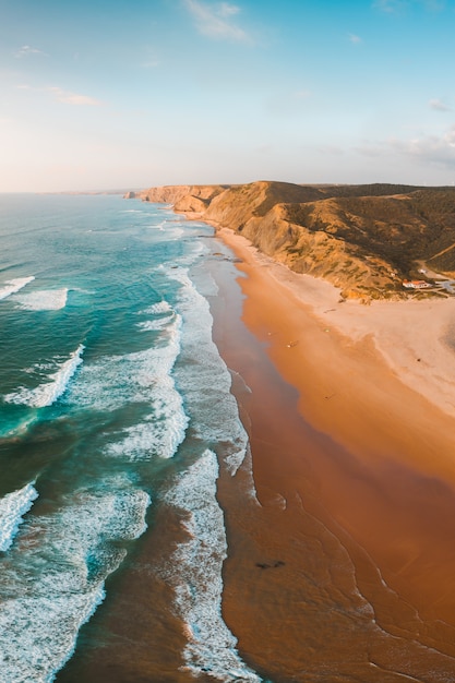 Colpo verticale delle onde dell'oceano mozzafiato e la spiaggia con scogliera rocciosa sotto il cielo blu