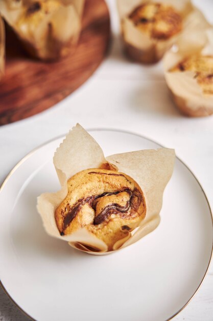 Colpo verticale di alto angolo di un delizioso muffin al cioccolato vicino a un piatto di legno su un piatto bianco