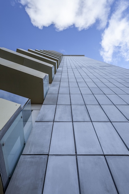 Colpo verticale di angolo basso di un edificio alto con i balconi di vetro sotto il bello cielo blu