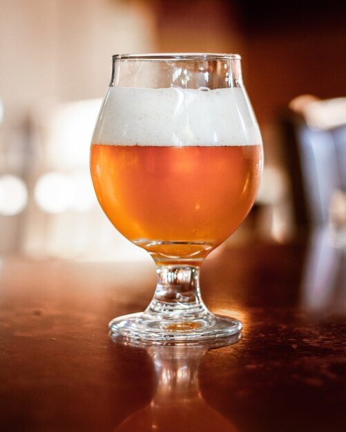 Colpo verticale di birra in una tazza di vetro con uno sfondo sfocato