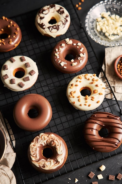 Colpo verticale di deliziose ciambelle ricoperte di glassa di cioccolato bianco e marrone su un tavolo nero