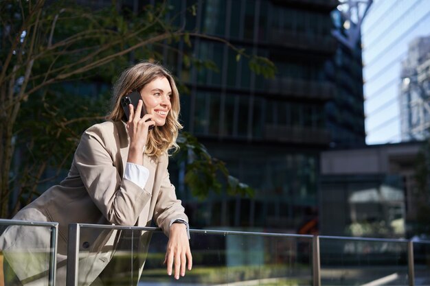 Colpo verticale di donna d'affari su una chiamata in piedi fuori dal centro affari che parla sul telefono cellulare