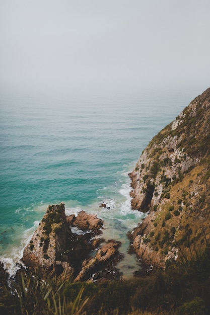 Colpo verticale di grandi rocce a Nugget Point Ahuriri, Nuova Zelanda con uno sfondo nebbioso