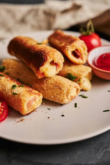 Colpo verticale di pane tostato rotoli con prosciutto e formaggio e pomodori e ketchup su un piatto bianco