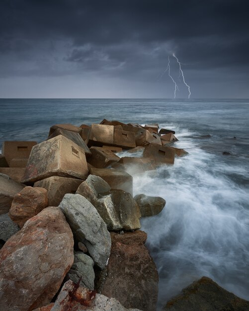 Colpo verticale di rocce in mare durante un temporale e fulmini
