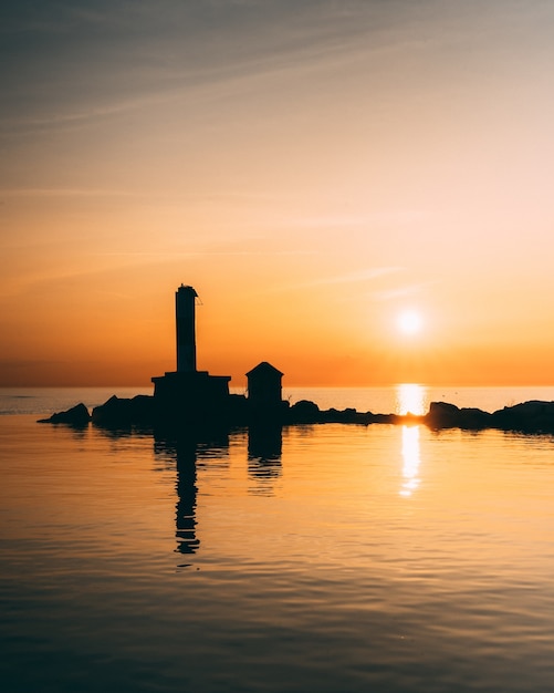 Colpo verticale di sagome degli edifici nel mezzo di un oceano calmo durante il tramonto