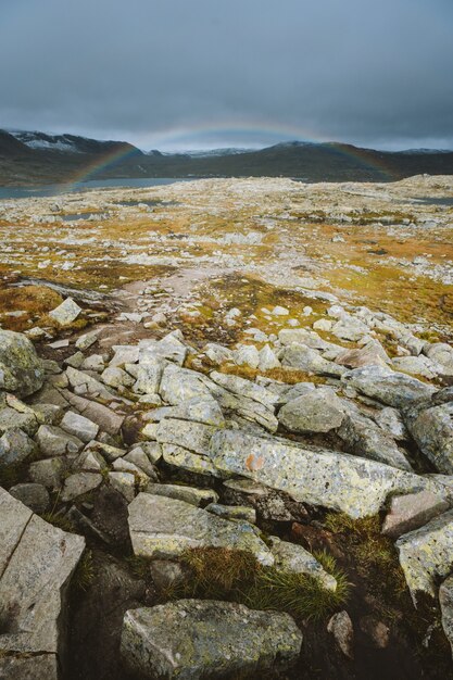 Colpo verticale di terra con molte formazioni rocciose e l'arcobaleno sullo sfondo a Finse, Norvegia