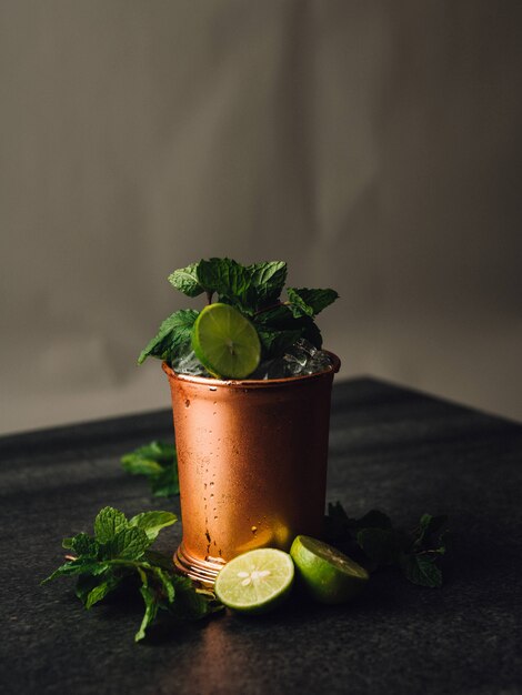 Colpo verticale di un cocktail mojito I una tazza di rame con foglie di limone e menta intorno ad esso