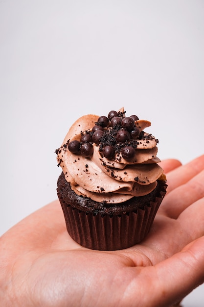 Colpo verticale di un cupcake al cioccolato sulla mano d'uomo su uno sfondo bianco