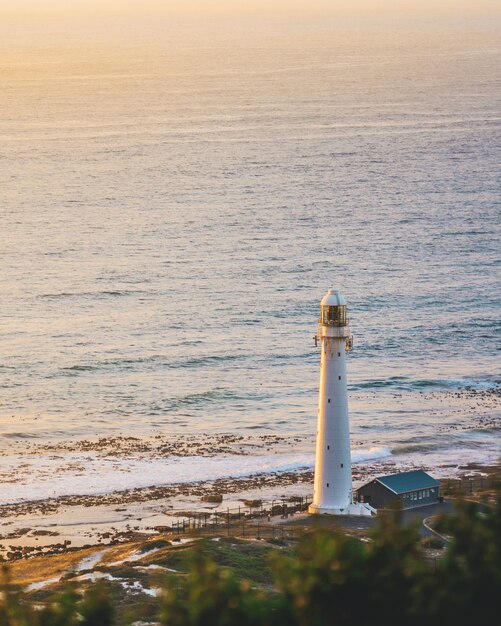 Colpo verticale di un faro bianco su una bellissima riva vicino a un specchio d'acqua.