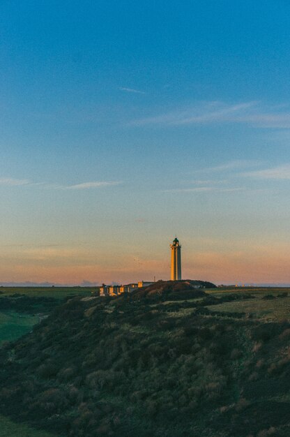 Colpo verticale di un faro in cima a una collina sotto un cielo al tramonto