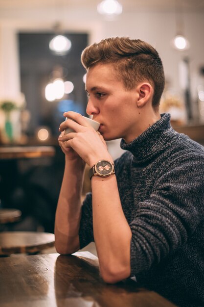 Colpo verticale di un giovane uomo che beve il caffè nella caffetteria