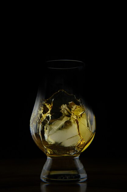 Colpo verticale di un liquido colorato dorato schizzi in un bicchiere isolato
