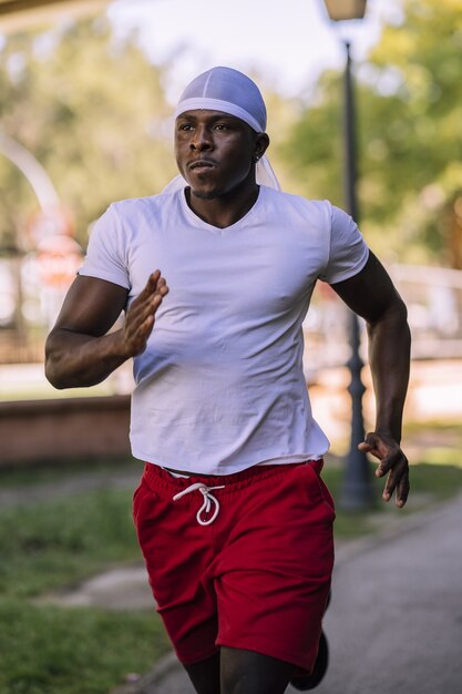 Colpo verticale di un maschio afro-americano in una camicia bianca fare jogging al parco durante il giorno